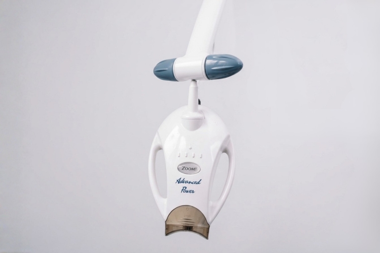 Lámpara de blanqueamiento dental suspendida sobre fondo blanco.