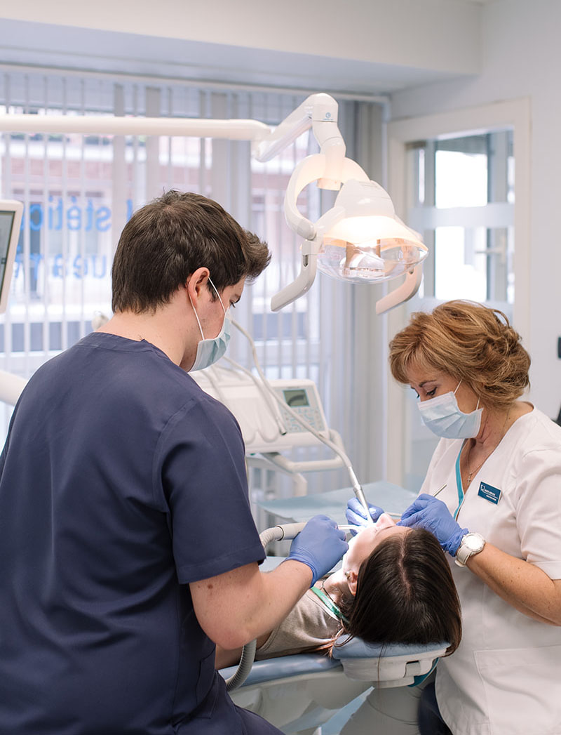 Dos profesionales atienden a una paciente en un sillón de clínica dental durante un tratamiento.
