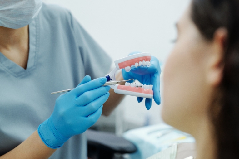 Profesional dental con guantes azules mostrando una maqueta de dientes a una paciente en consulta.
