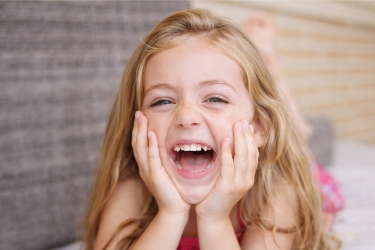 Niña sonriendo con la boca abierta y las manos en el rostro en un retrato de primer plano.