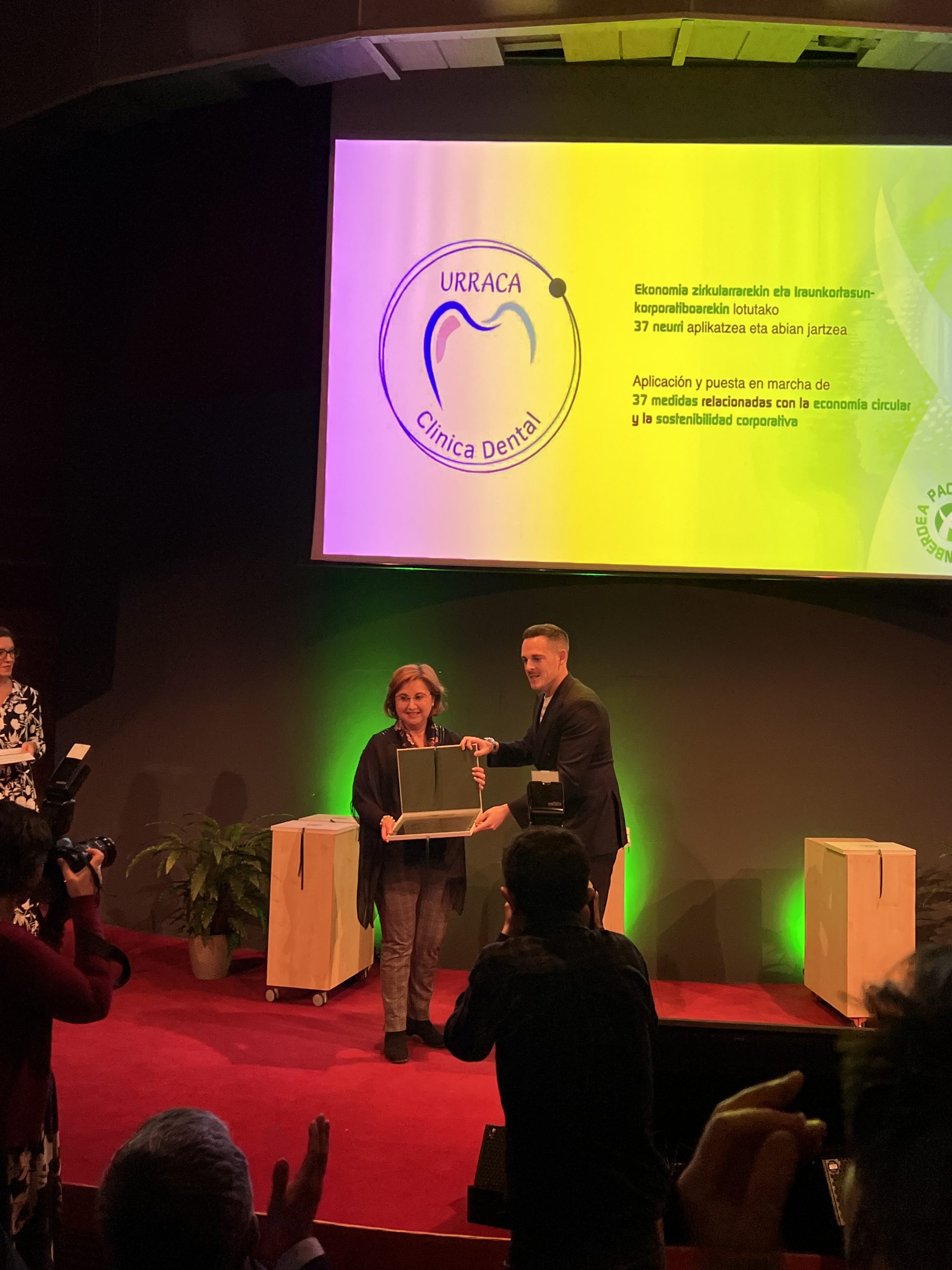 Entrega de premio medioambiental en un escenario con pantalla de presentación al fondo.