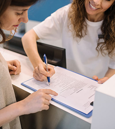 Paciente y profesional revisando y firmando documentación en recepción durante una primera consulta.