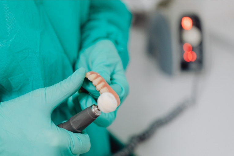 Prótesis dental sostenida con guantes mientras se trabaja con una pieza de mano en consulta.