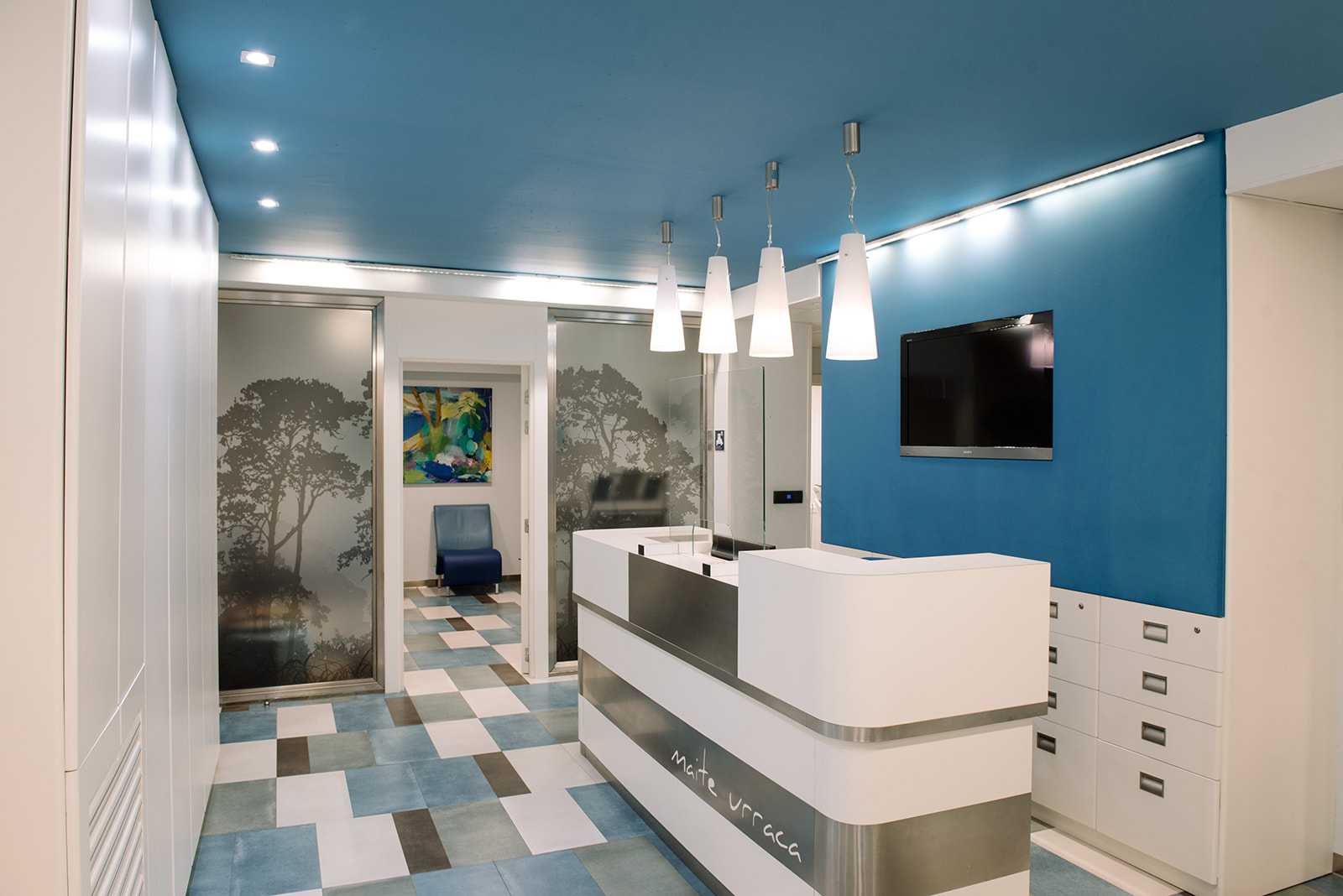 Recepción de clínica dental con mostrador blanco, pared azul y sala al fondo.