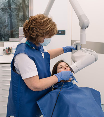 Profesional dental realiza una radiografía intraoral a una paciente durante tratamientos dentales en consulta.
